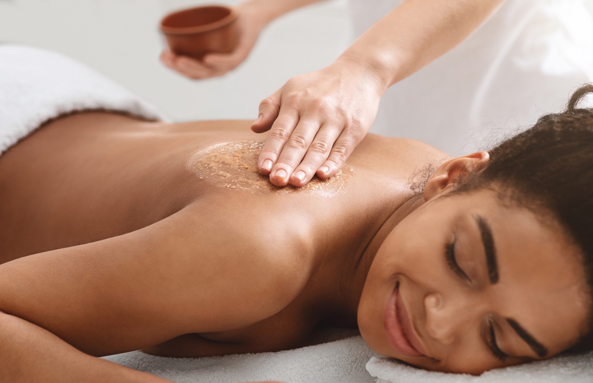 Masseuse applying body scrub on black girl back