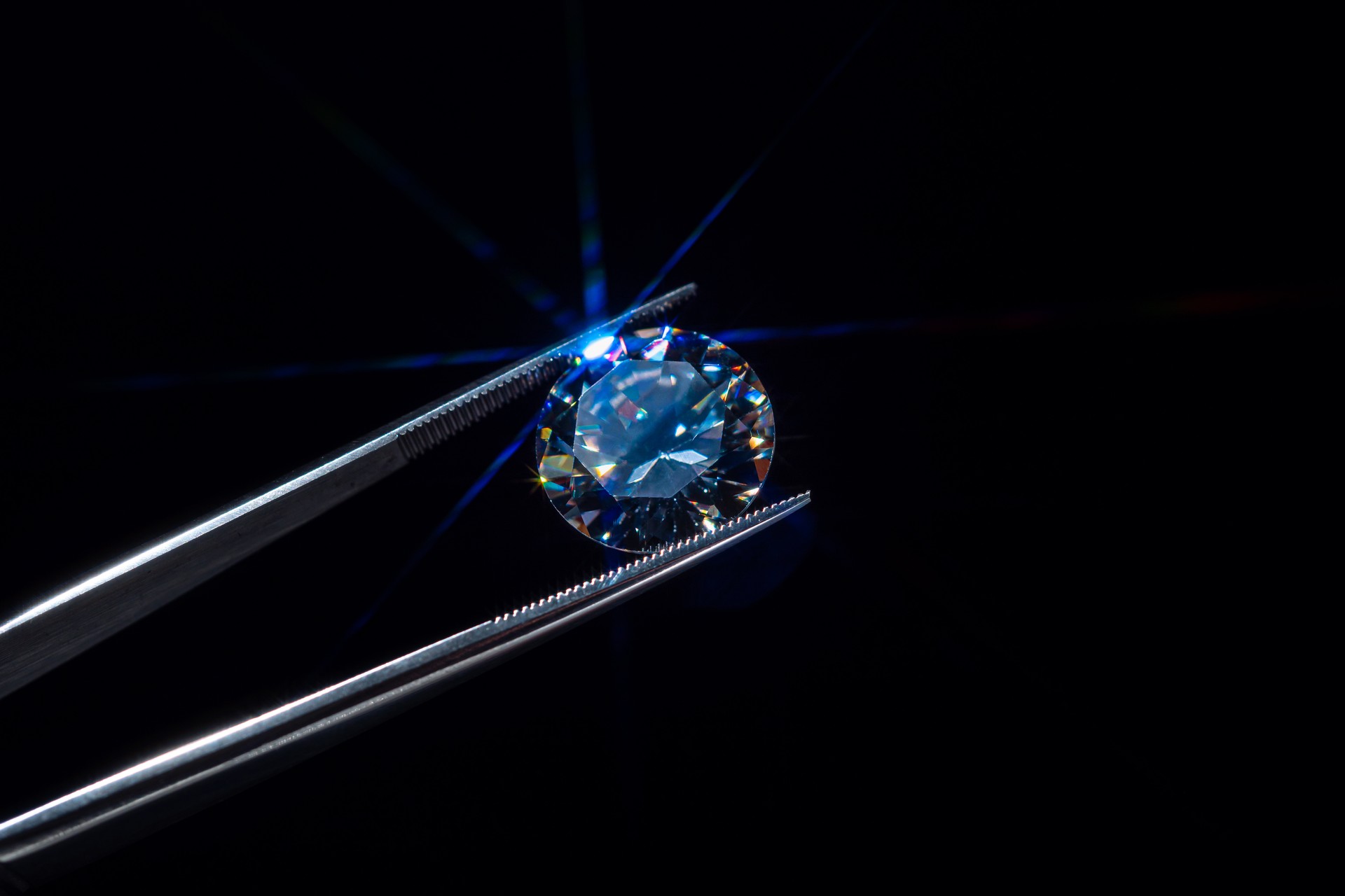 Loose diamond in tweezers selective focus. Macro shot of precious stone inspection for defects. Certification of brilliant cut diamond. Gemstone in clamp for making luxury jewelry. Natural material.