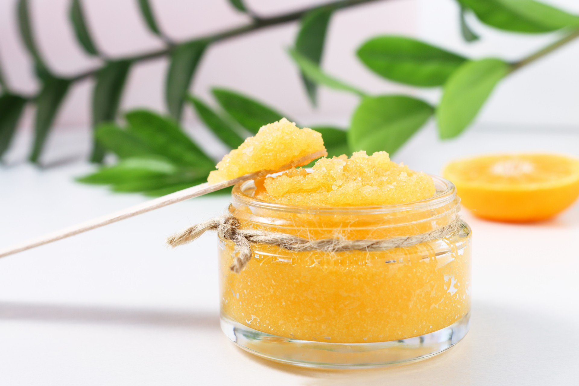 Body scrub with citruses front view. Cosmetic product for spa procedures and skin cleansing on a wooden table with green leaves of the plant