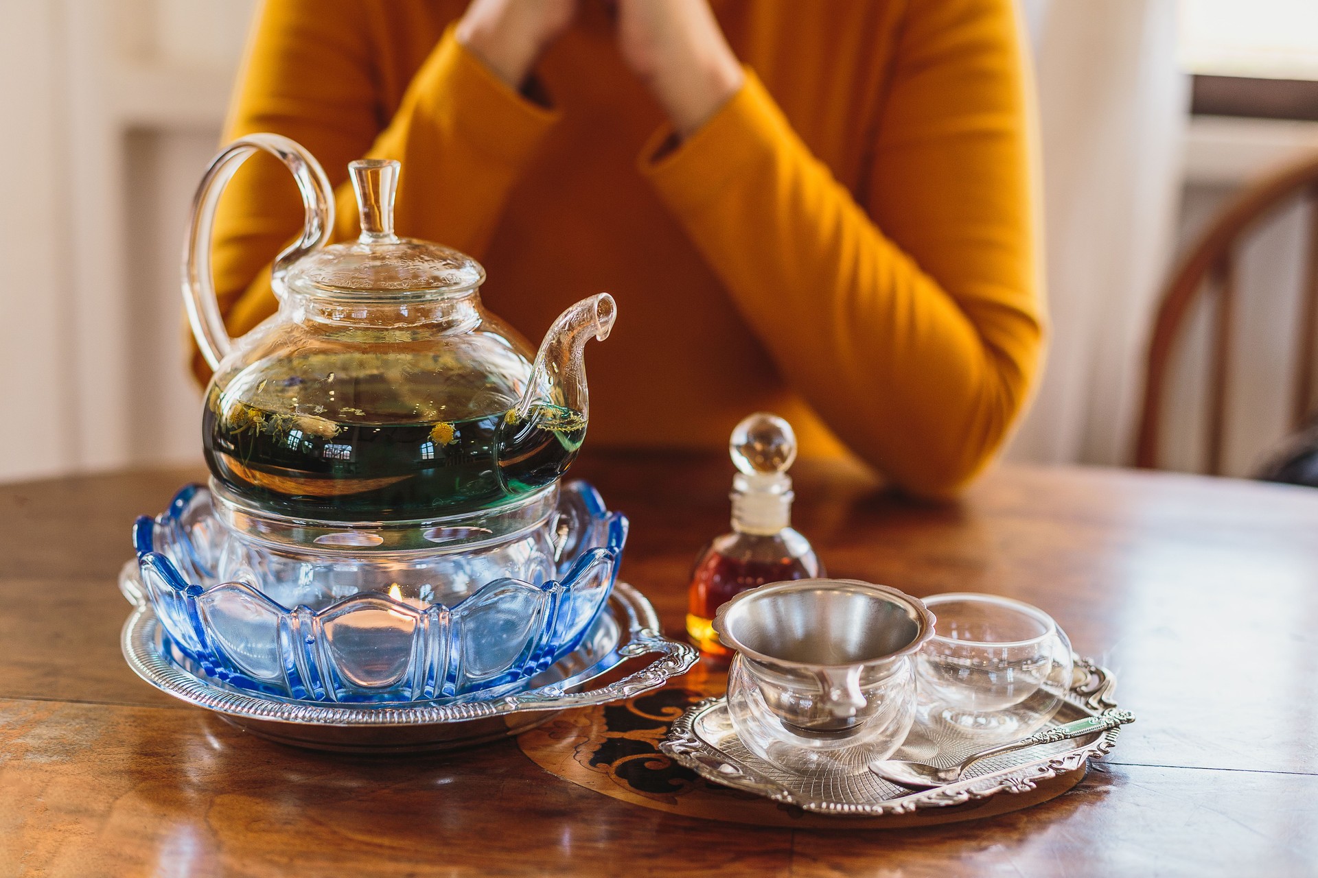 Tea ceremony concept, Woman sitting in front of glass teapot and tea cups with Syrup bottle on wooden table at home