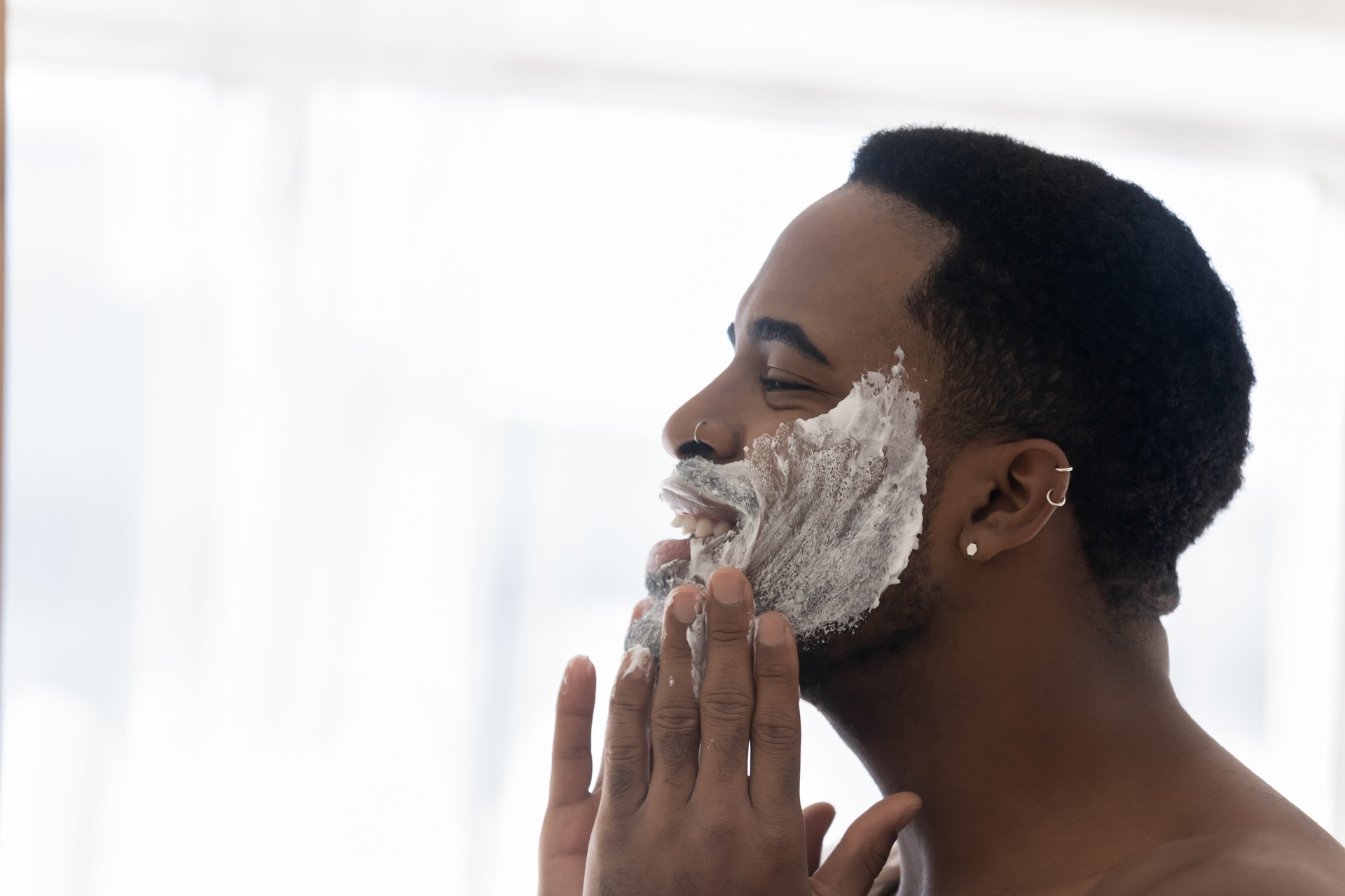 Happy young mixed race man cleansing face with foamy scrub.