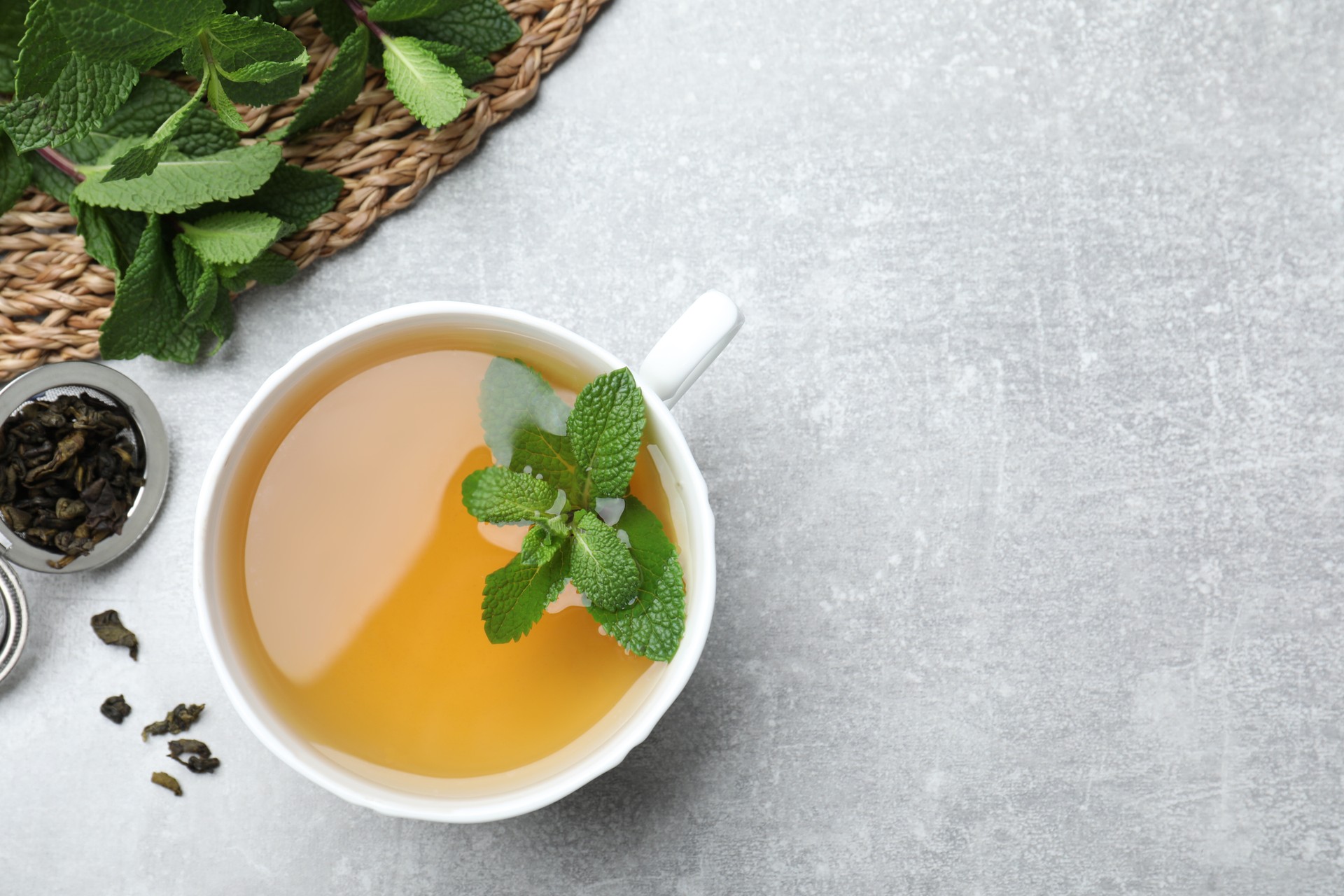 Cup of aromatic green tea with mint and dry leaves on grey table, flat lay. Space for text