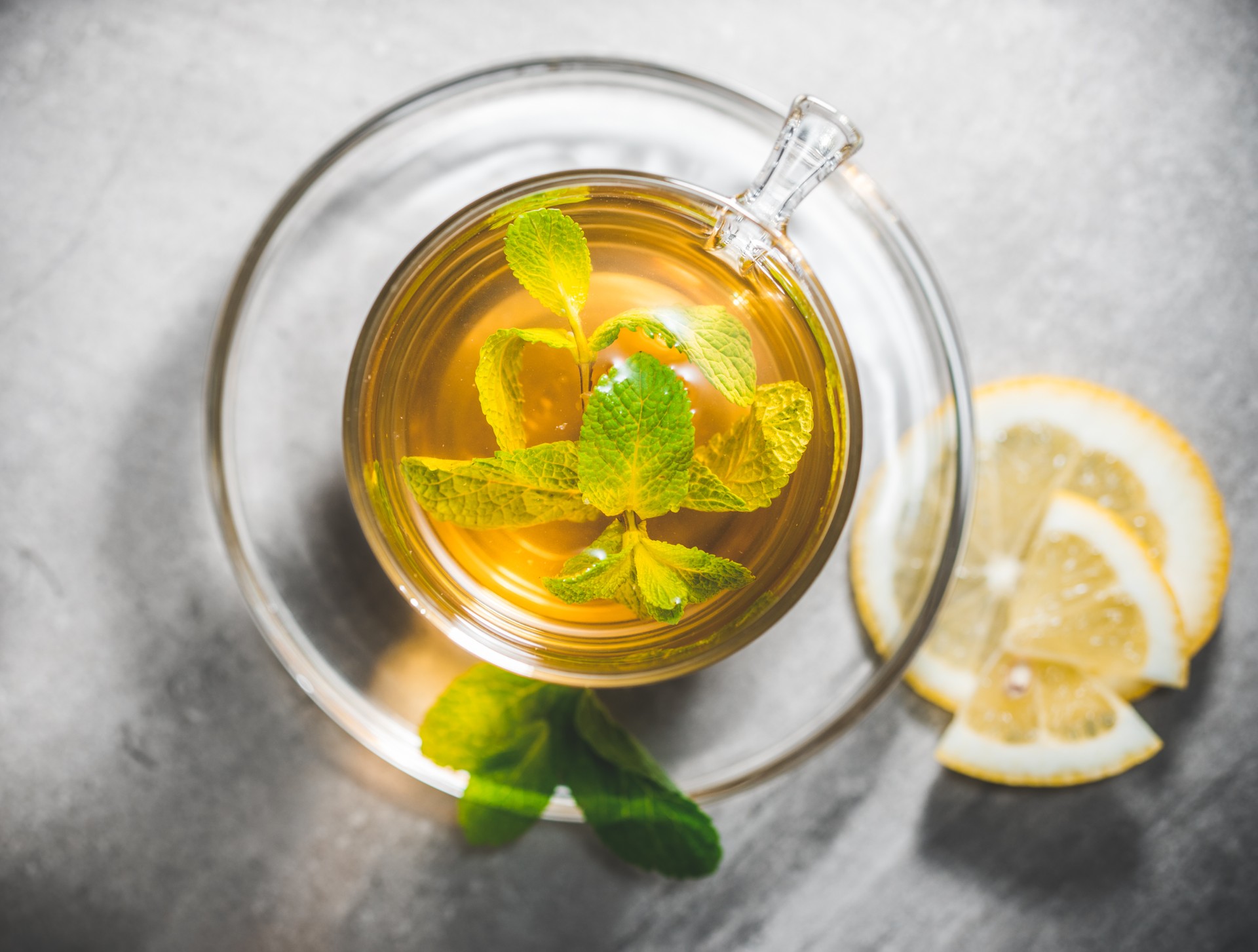 Glass cup of mint tea leaves with fresh slice lemon on gray table. Topview, above.