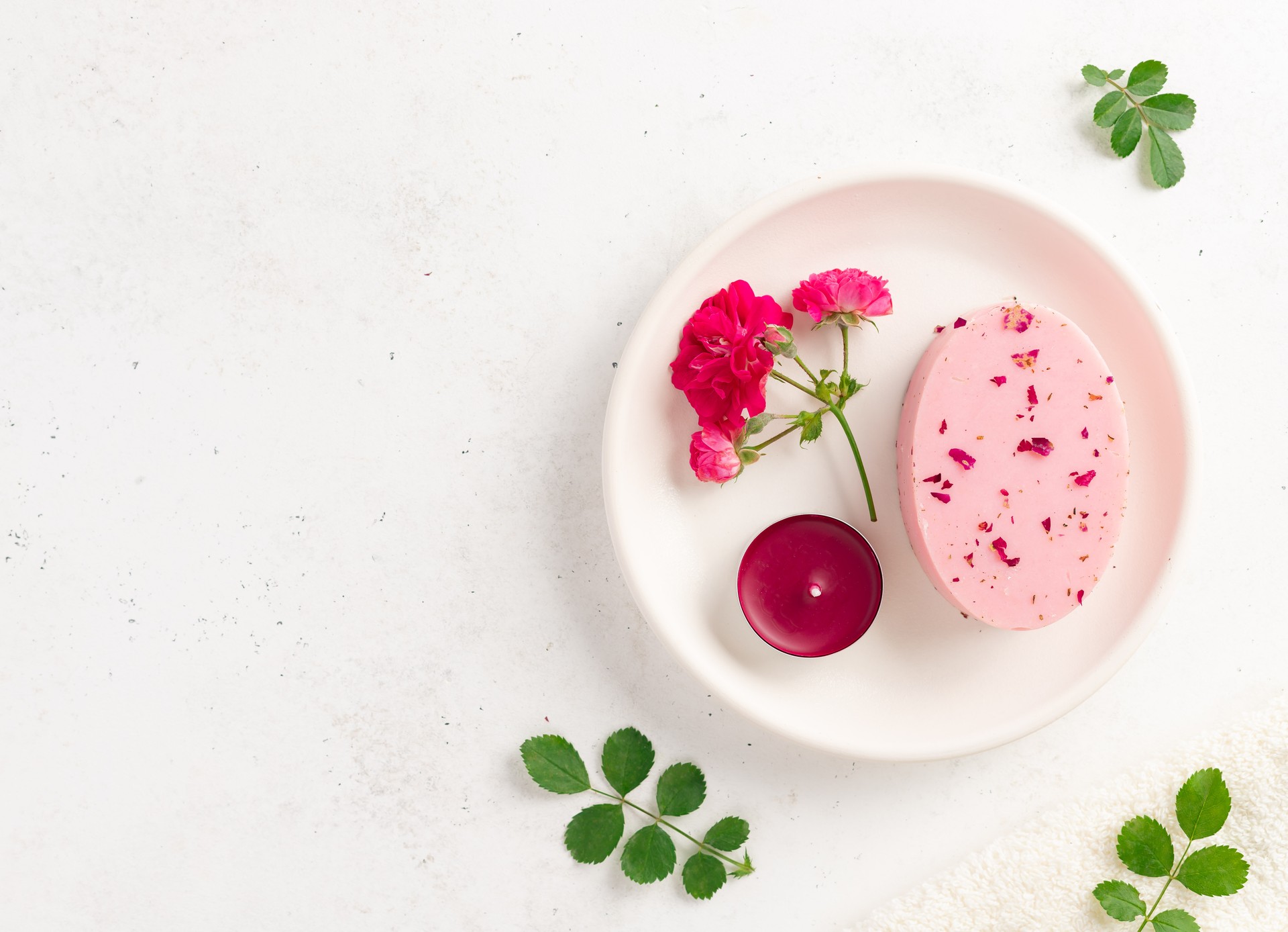 spa background with bar of soap with dried rose petals, fresh roses, candle and green leaves. skin care concept.